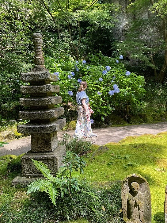 Student in white dress walking down path in Japanese garden with stone statue in foreground