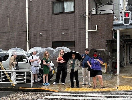 Groups of students waiting outside with umbrellas
