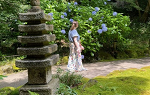 Student in white dress walking down path in Japanese garden with stone statue in foreground