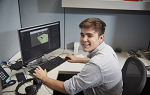 Landmark College alumnus Bobby Christopher smiles for camera while working at computer during his internship at Hasbro.