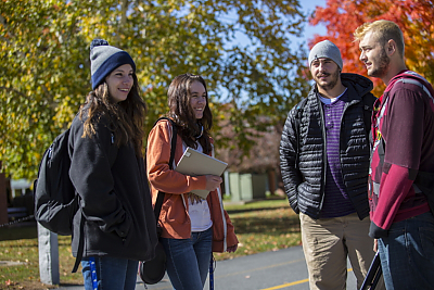 Four Landmark College students stand outdoors with fall foliage in background